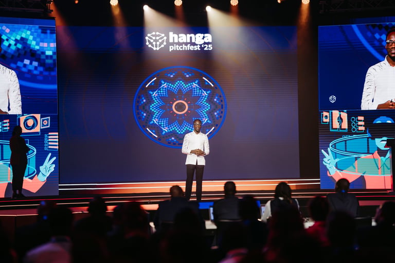 Presenter on stage at Hanga Pitches 2025 conference with large blue digital globe display and audience seated in foreground