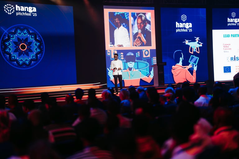 Conference stage with presenter and large screens displaying Hanga Pitches 23 branding and digital content before an audience
